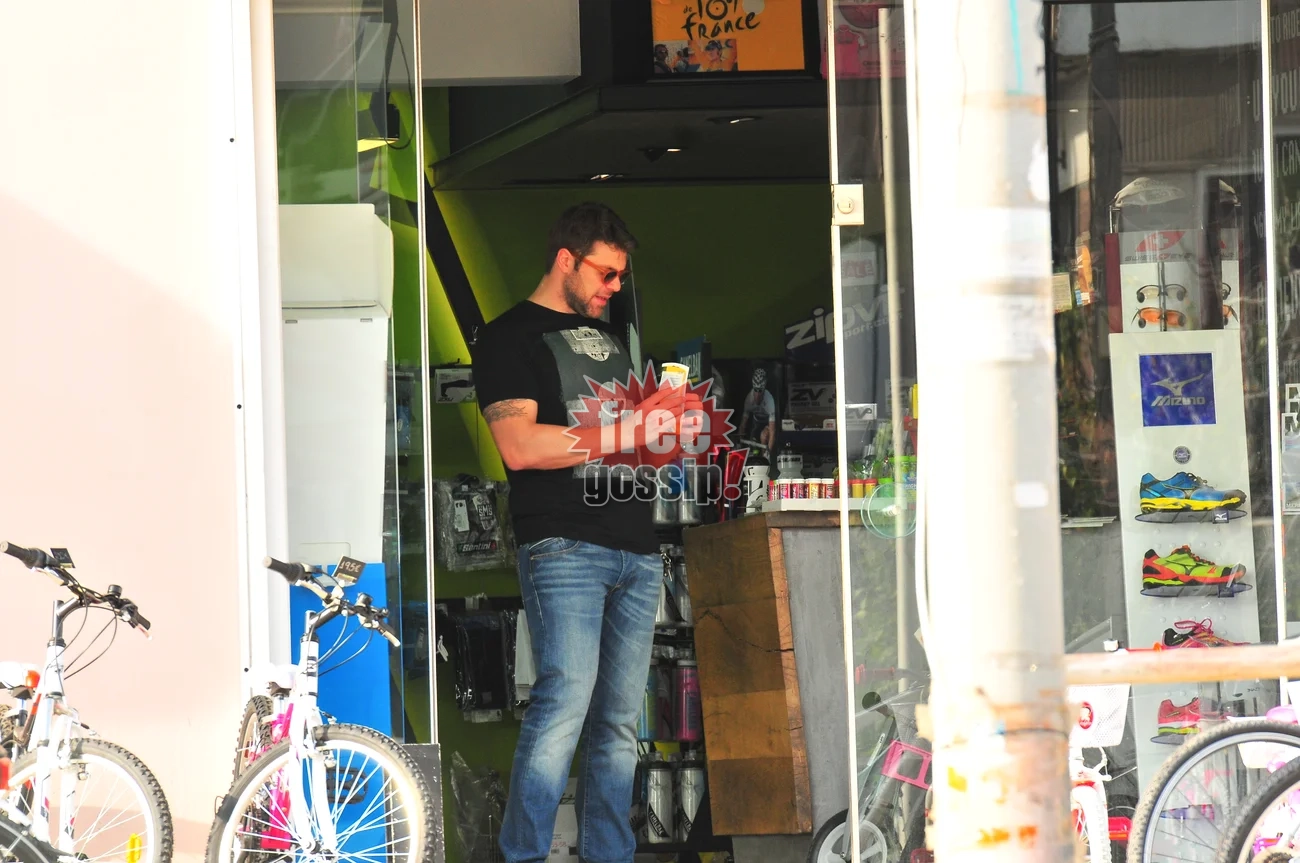 Ο Χρήστος Χολίδης με μαύρο μπλουζάκι και τζιν παντελόνι κοιτάζει ένα προϊόν μέσα σε κατάστημα ποδηλάτων