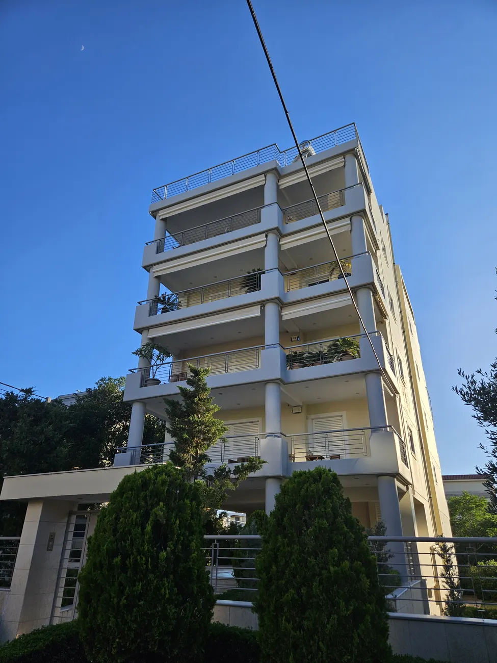 Γωνιακή όψη σύγχρονης πενταώροφης πολυκατοικίας με μπεζ και γκρι αποχρώσεις